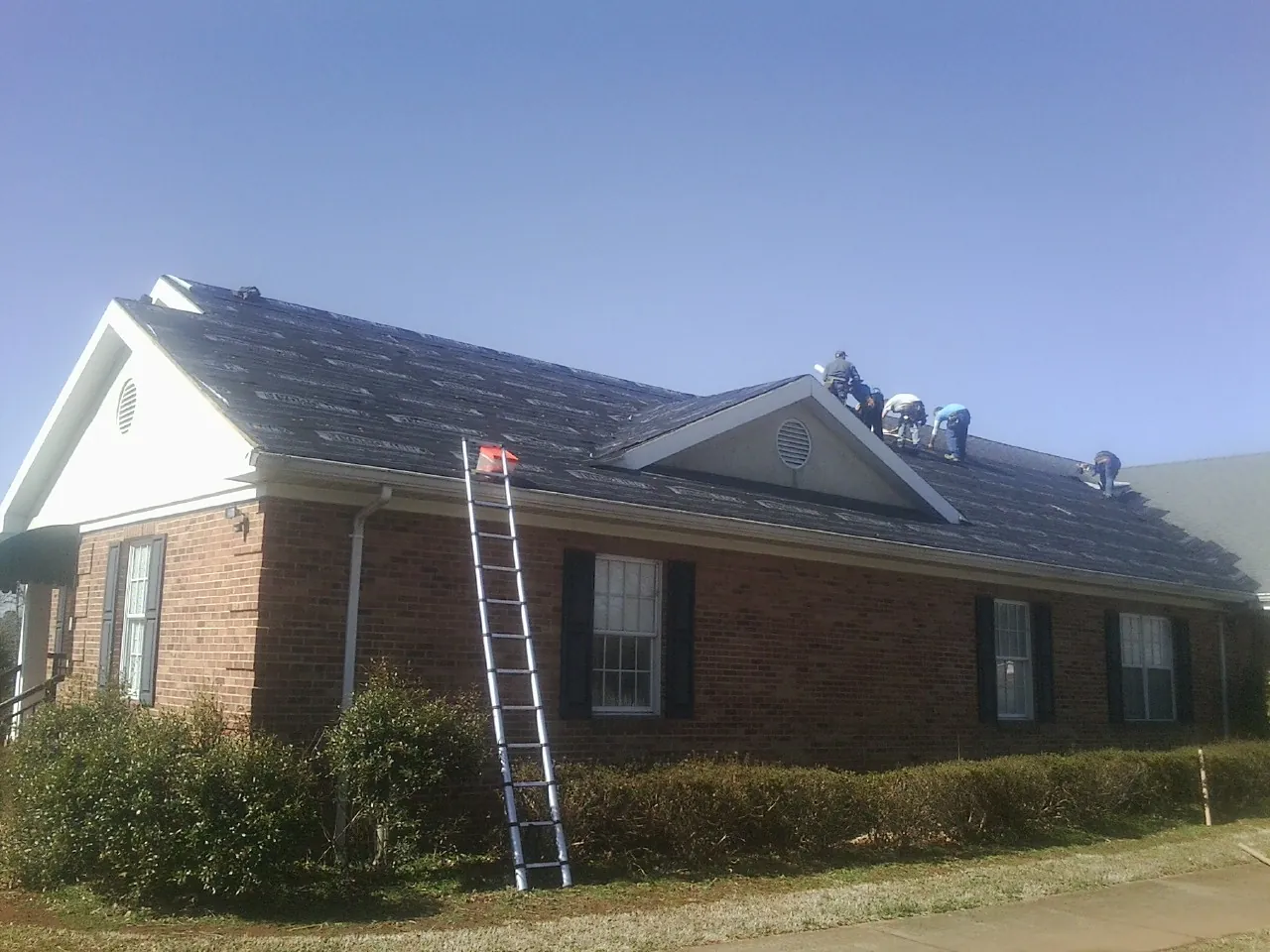 Crew tearing shingles off a brick ranch roof with a ladder set — Metal Roof Repair work by our crew in Bayside