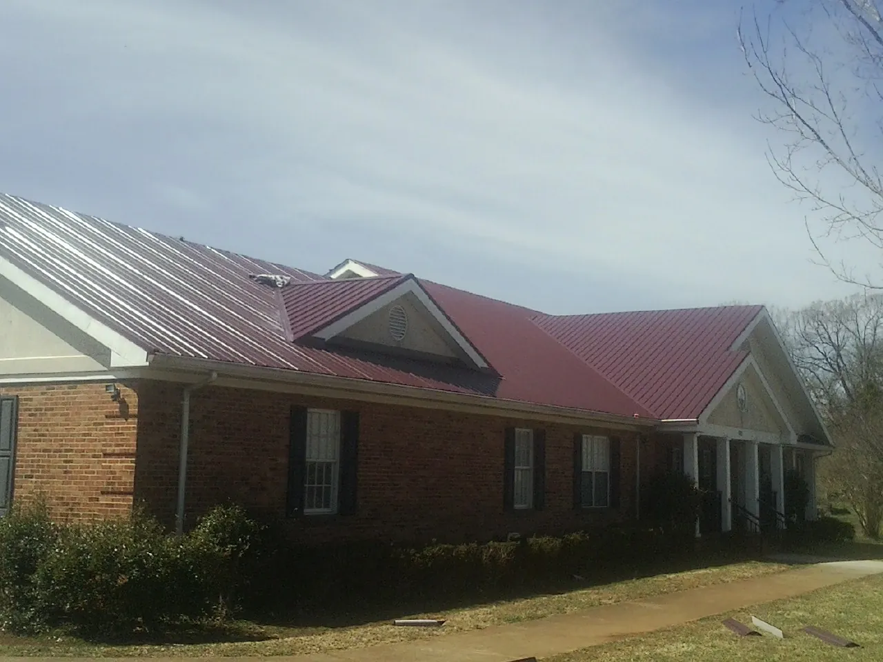 Red metal roof with gabled entries on a long brick building, from a Hail Damage Roof Repair job in Bayside