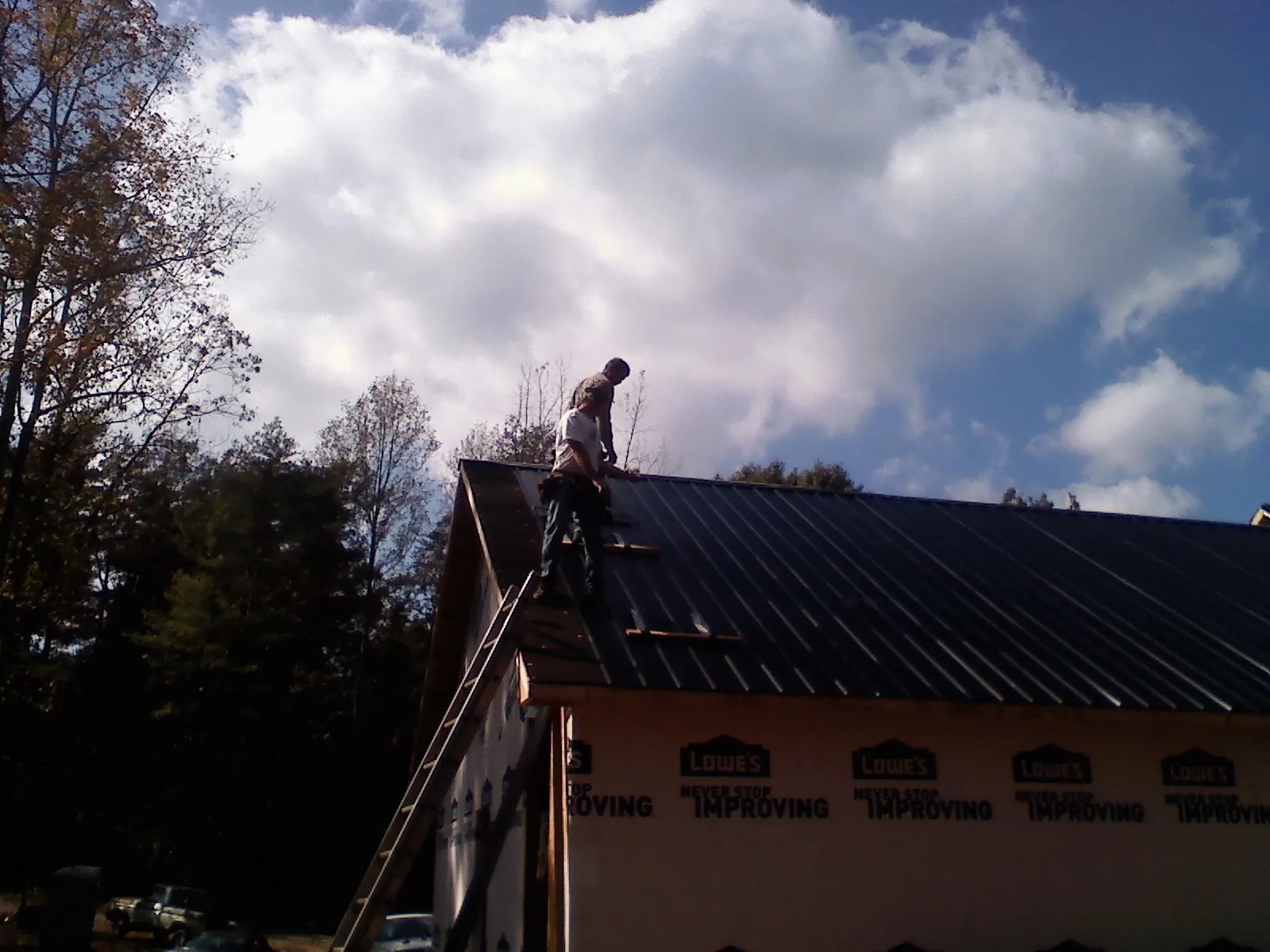 Roofer fastening dark metal panels high against a cloudy sky, from a Roof Inspection job in Bayside