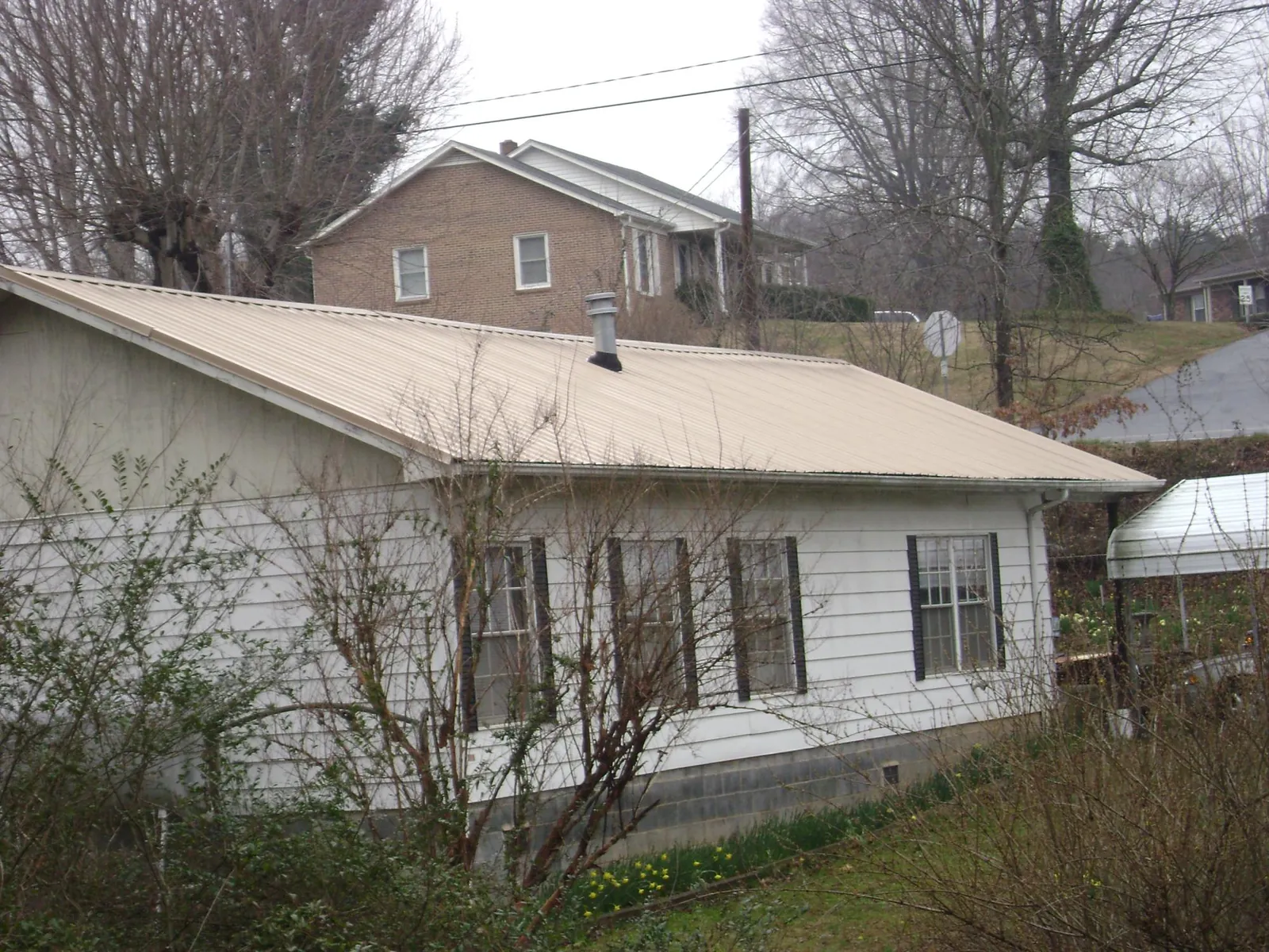 Tan metal roof on a white sided house set into a hillside — Commercial Roofing by Roofing Brothers in Bayside