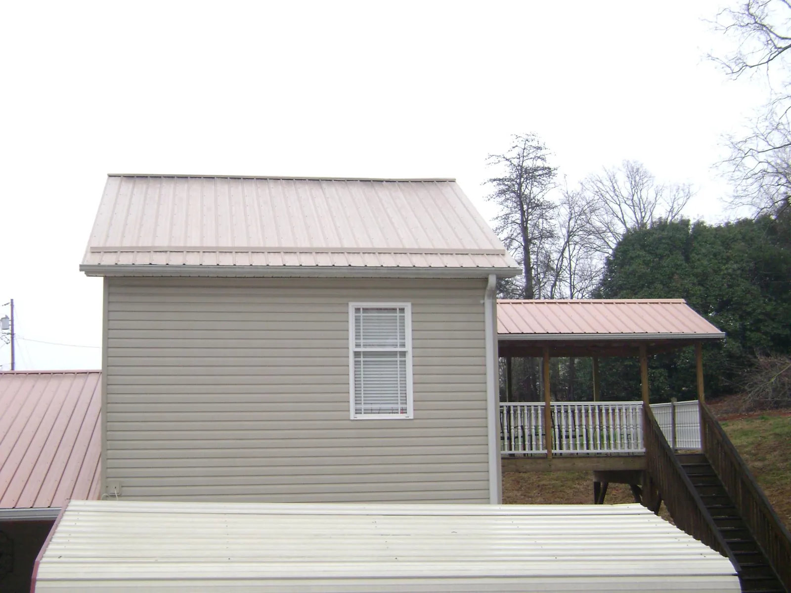 Tan metal roofs on a two story addition and attached porch, from a Roof Replacement job in Bayside
