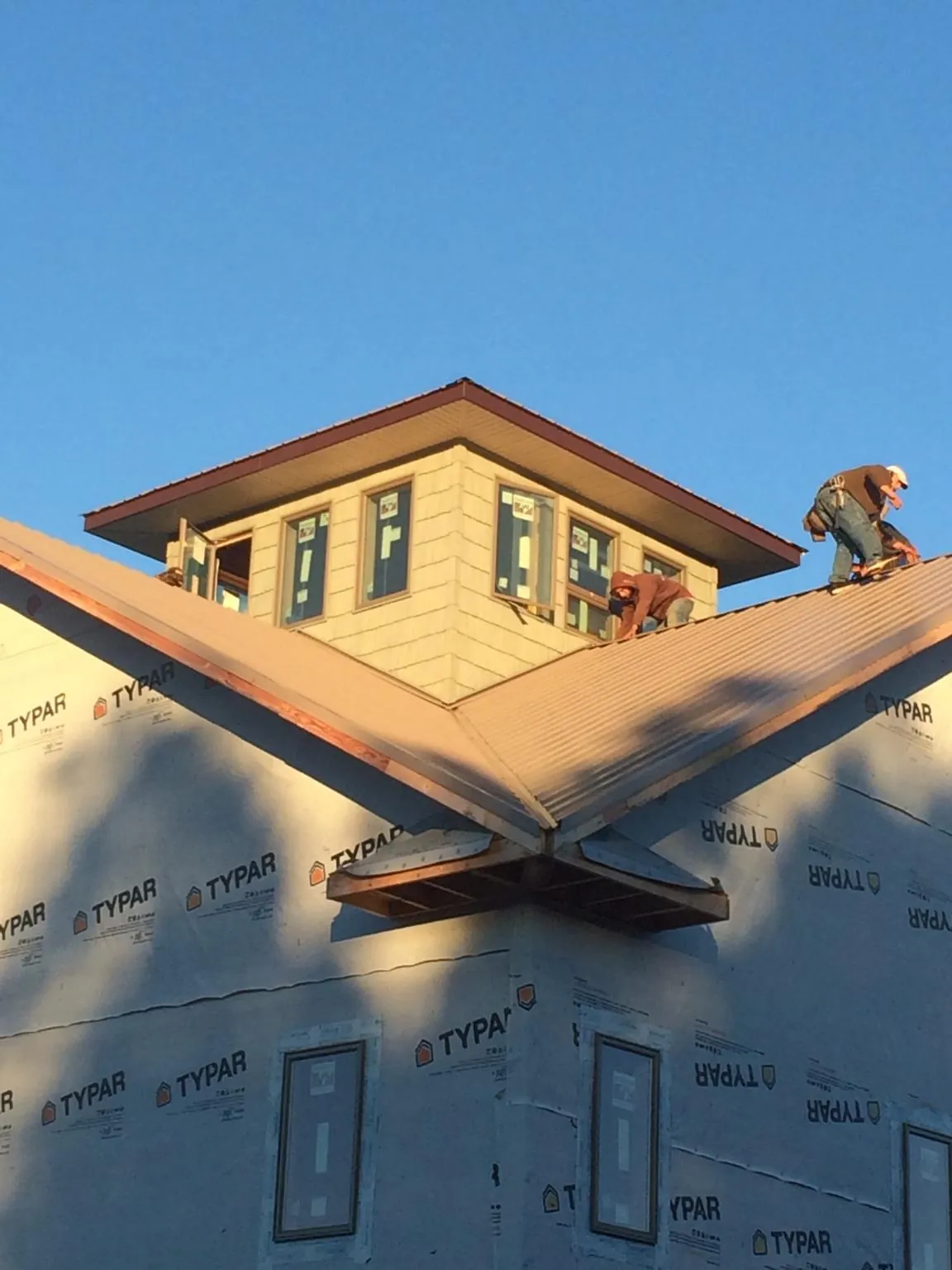 Roofers working around a rooftop cupola on a new metal roof at sunset — Roof Waterproofing in Bayside by Roofing Brothers